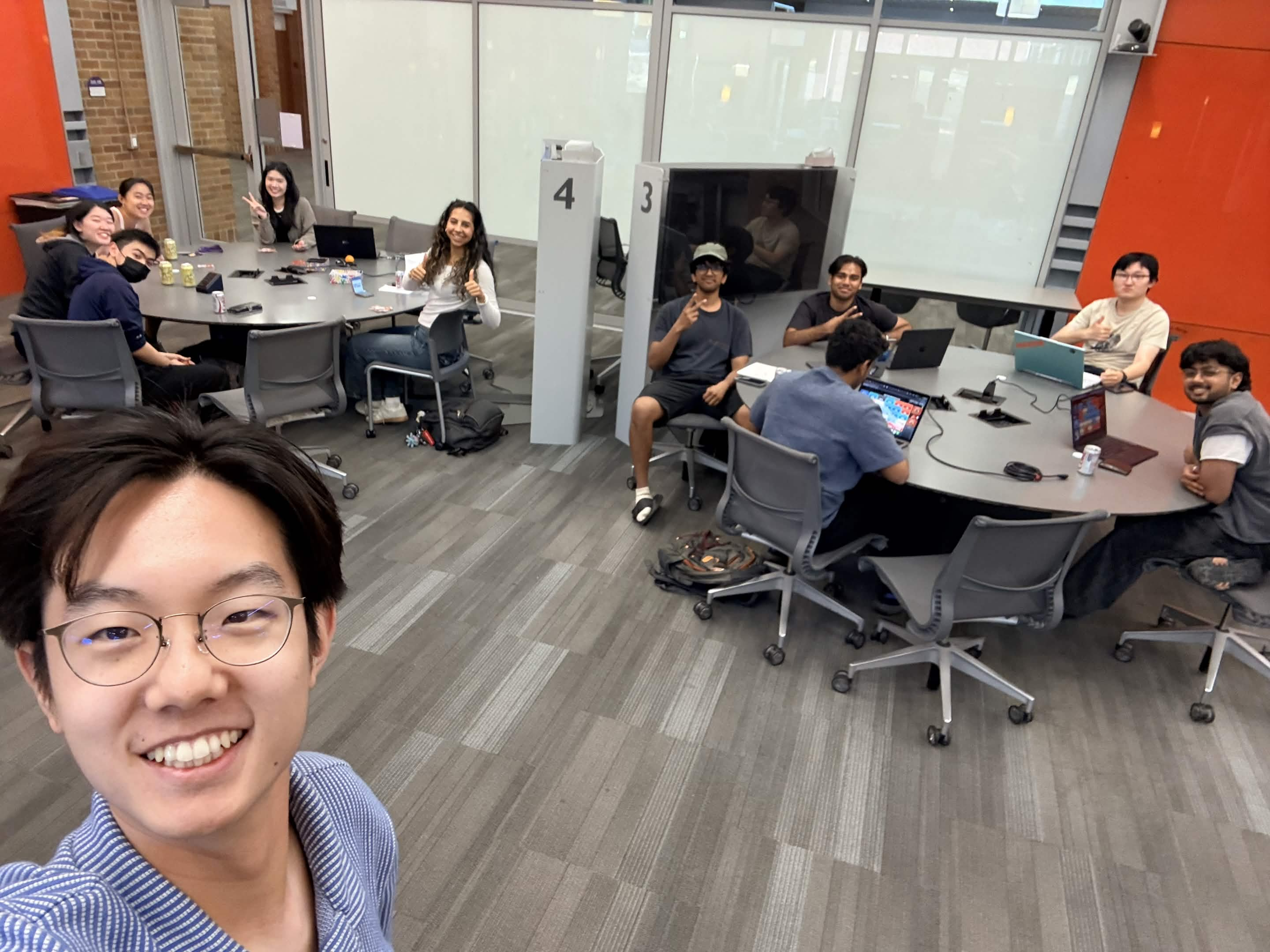 Math AI Lab members seated at tables with laptops, smiling for a selfie at the summer 2026 social